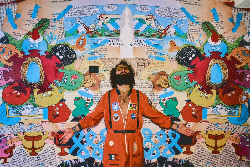 Alejandro in orange suit in front of monumental collage