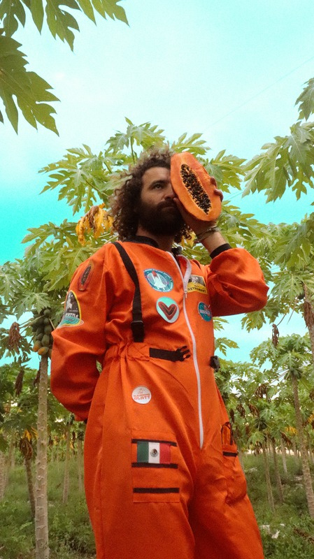 Alejandro Glatt in orange space suit among papaya trees
