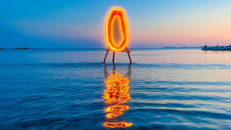 Neon papaya sculpture over the ocean at sunset